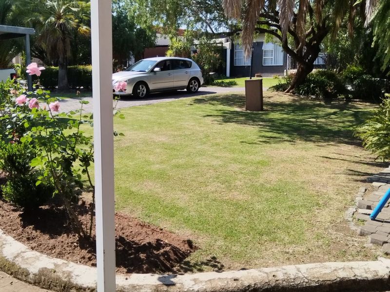 A view of a residential garden featuring a paved patio area, a retaining wall, and a well-maintained lawn with mature trees.