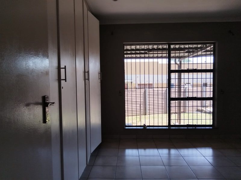 A spacious bedroom featuring tiled flooring, built-in cupboards, and a window fitted with security bars, offering a functional and secure living space.