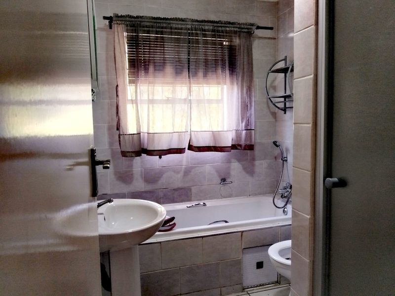 A functional bathroom featuring a pedestal basin, a built-in bathtub with a handheld shower mixer, and tiled wall finishes.