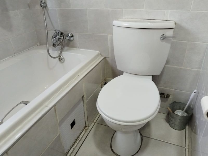 A functional bathroom featuring a standard bathtub with shower mixer and a white toilet, finished with neutral wall and floor tiling.