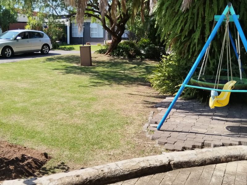 A residential garden area featuring a paved walkway, established lawn, and mature trees, providing a functional outdoor space.