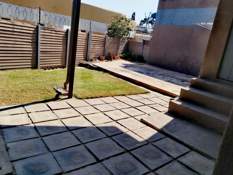 A private rear courtyard featuring a paved patio area, concrete steps, a small lawn, and secure perimeter walling with razor wire.