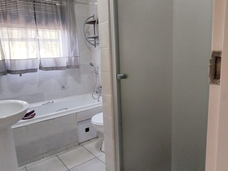 A functional bathroom featuring a bathtub, pedestal basin, and a separate shower enclosure with tiled finishes throughout.