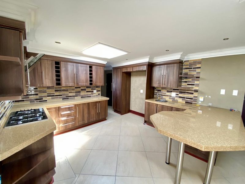 Spacious kitchen featuring dark wood cabinetry, stone countertops, a gas hob, integrated extractor, and a breakfast bar with a mosaic tile backsplash.