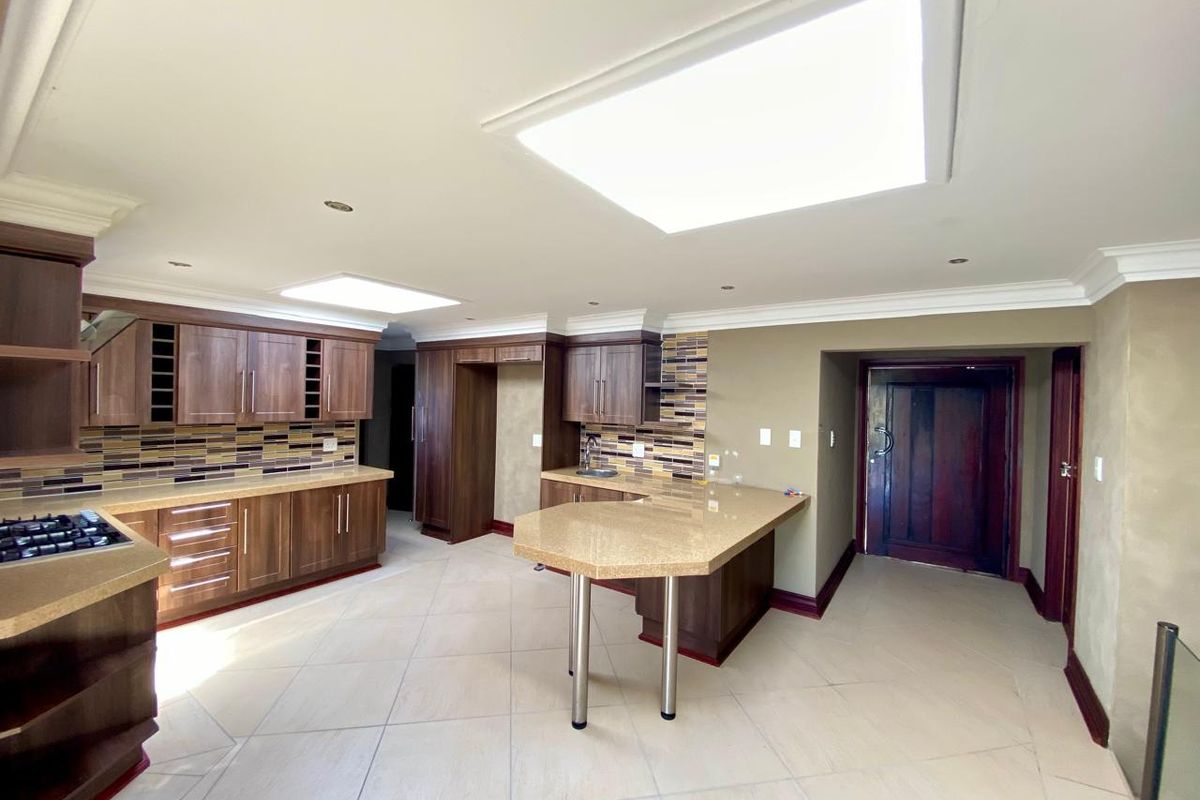 Spacious kitchen featuring dark wood cabinetry, stone countertops, a breakfast bar, mosaic backsplash, and dual skylights providing ample natural light.