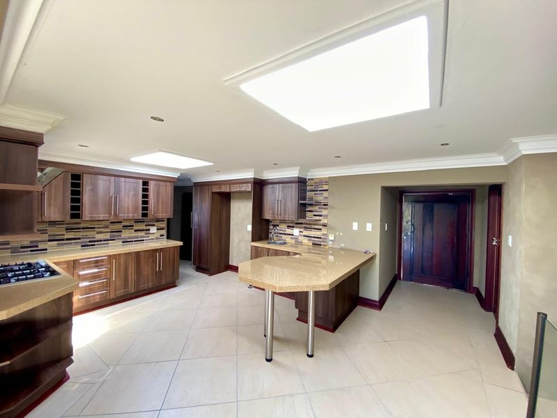 Spacious kitchen featuring dark wood cabinetry, stone countertops, a breakfast bar, mosaic backsplash, and dual skylights providing ample natural light.