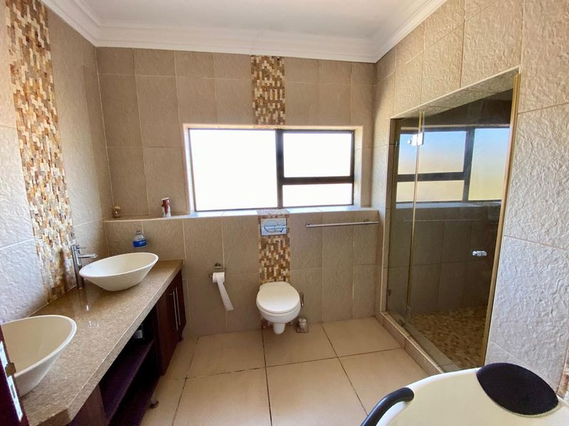 Modern bathroom featuring a double vanity with vessel sinks, stone countertop, wall-mounted toilet, and a glass-enclosed shower with decorative tiled accents.