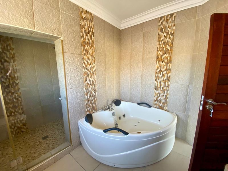 Modern bathroom featuring a corner spa bath, a separate walk-in shower, and decorative mosaic tile accents on the walls.