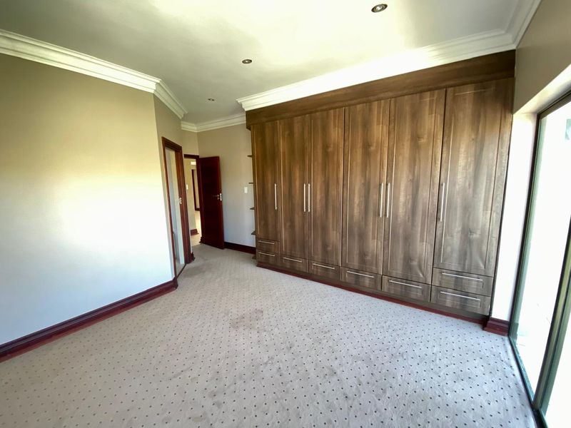Spacious bedroom featuring extensive built-in wooden cupboards, neutral carpeting, and recessed ceiling lighting, offering a clean and functional living space.