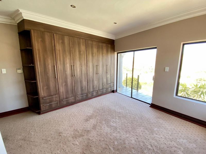 Spacious bedroom featuring extensive built-in wooden cupboards, carpeted flooring, and a sliding glass door providing access to an outdoor area.