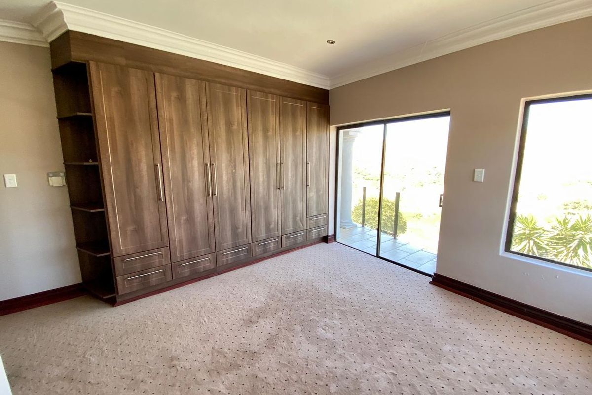 Spacious bedroom featuring extensive built-in wooden cupboards, carpeted flooring, and a sliding glass door providing access to an outdoor area.