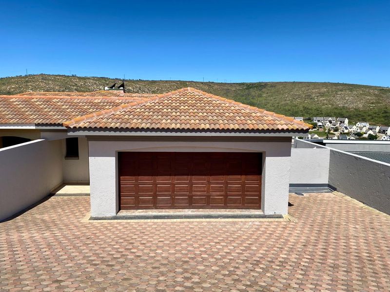 A well-maintained garage featuring a wooden sectional door, tiled roof, and paved driveway area within a residential duet property setting.