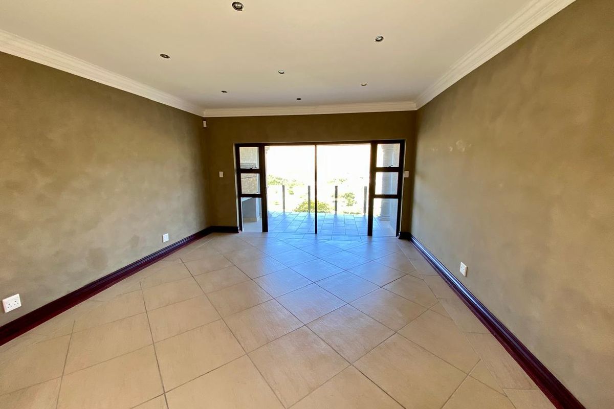 A spacious, empty living room featuring tiled floors, recessed lighting, and large sliding glass doors that open onto an outdoor patio area.
