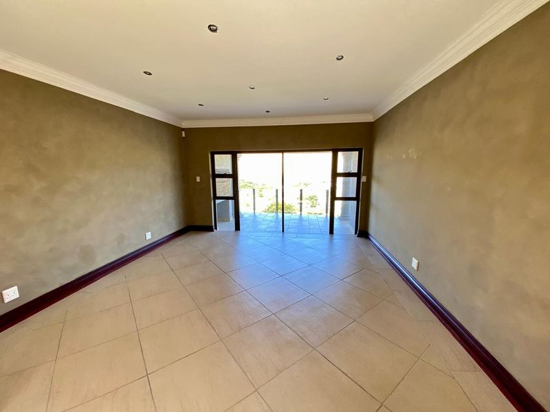 A spacious, empty living room featuring tiled floors, recessed lighting, and large sliding glass doors that open onto an outdoor patio area.