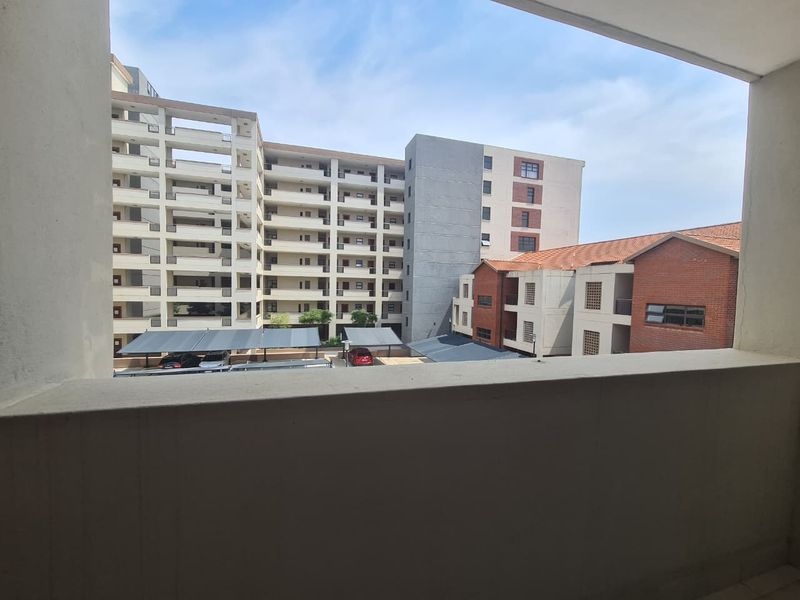 A view from a balcony overlooking the apartment complex courtyard, featuring covered parking bays and surrounding residential building facades.