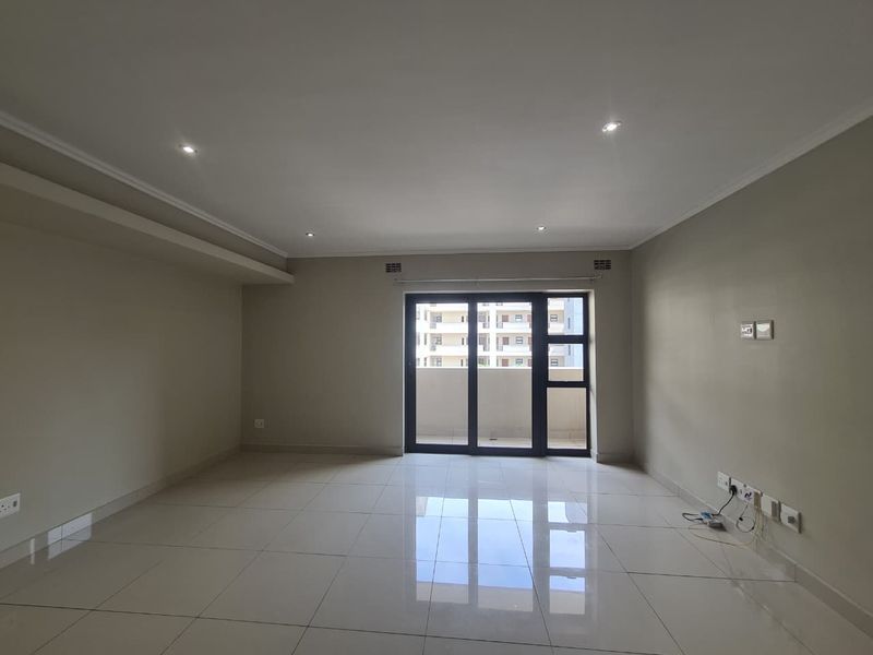 A bright, empty living room featuring neutral walls, polished tile flooring, recessed lighting, and a sliding glass door leading to an outdoor balcony.