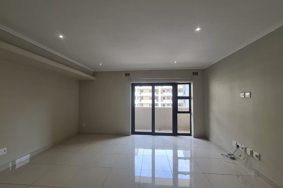 A bright, empty living room featuring neutral walls, polished tile flooring, recessed lighting, and a sliding glass door leading to an outdoor balcony.