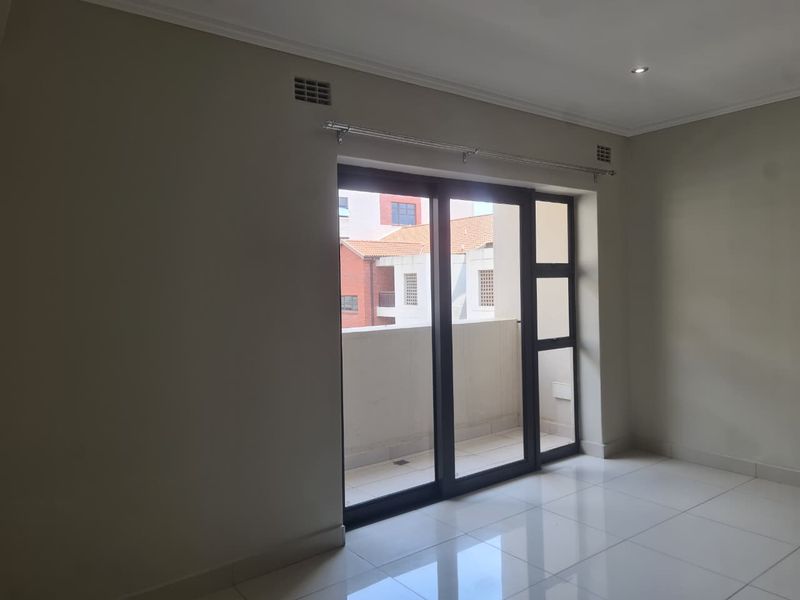 A bright, empty living room featuring neutral walls, polished tile flooring, and a large sliding glass door providing access to an outdoor balcony.
