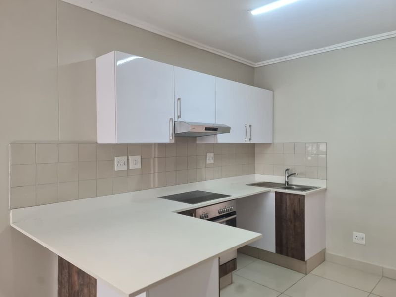 A modern, clean kitchen featuring white cabinetry, a built-in oven and hob, extractor fan, and a functional tiled backsplash with ample counter space.