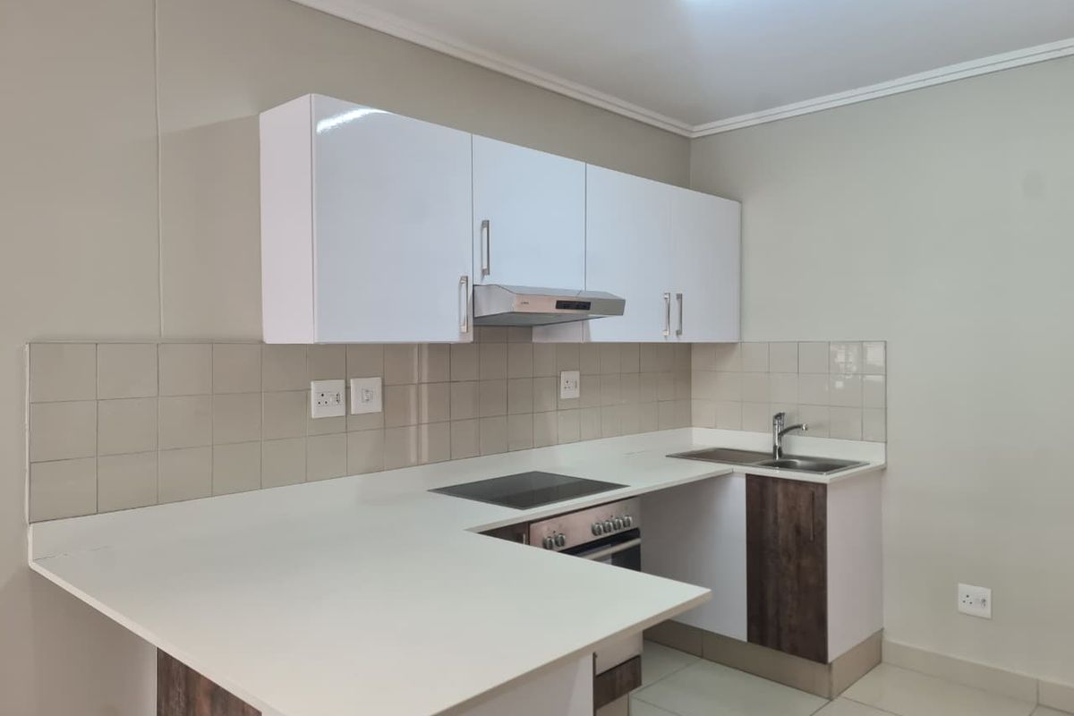 A modern, clean kitchen featuring white cabinetry, a built-in oven and hob, extractor fan, and a functional tiled backsplash with ample counter space.