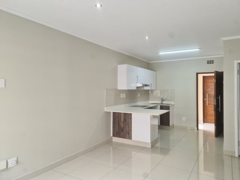 Modern open-plan kitchen featuring sleek cabinetry, integrated hob, and tiled flooring, offering a clean and functional space ready for personalization.