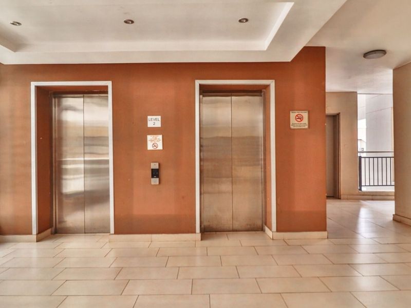 A clean and well-maintained apartment building hallway featuring dual stainless steel elevators and neutral tiled flooring.