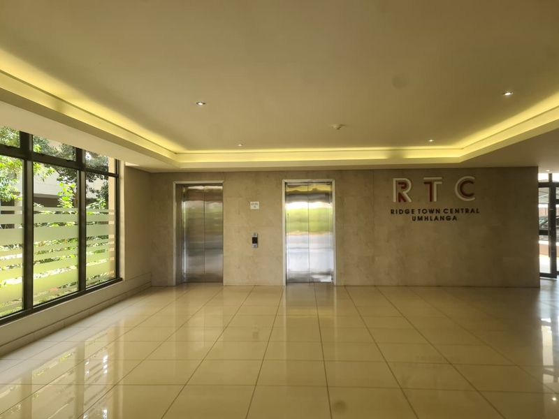 A modern, well-maintained apartment building lobby featuring tiled floors, recessed lighting, and dual elevator access.