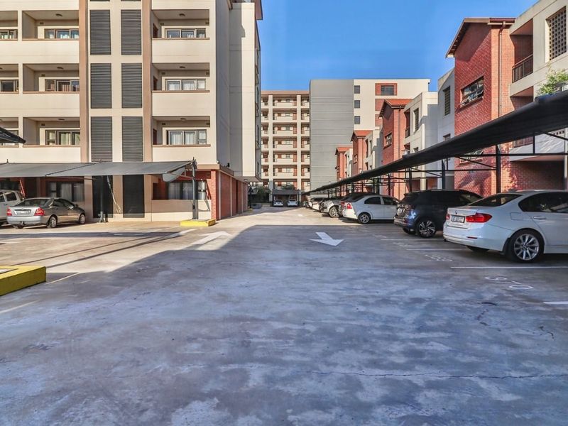 Exterior view of an apartment complex parking area featuring covered parking bays and multi-story residential buildings with brick and concrete finishes.