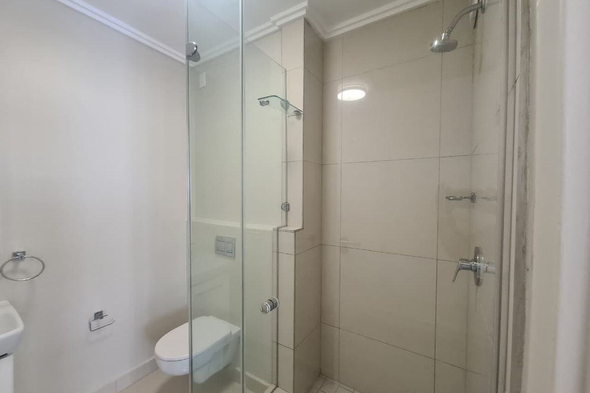 A clean and modern bathroom featuring a wall-mounted toilet and a glass-enclosed shower with neutral wall tiling.