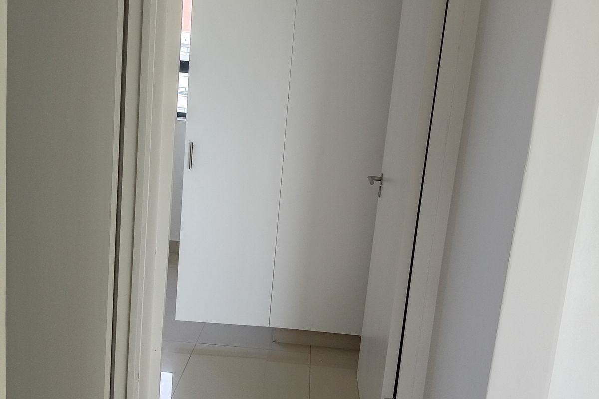 A clean, minimalist hallway featuring neutral tiled flooring and white built-in cupboards, providing a bright and functional transition space within the apartment.