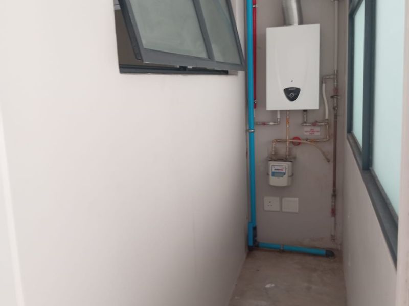 A functional utility space featuring a wall-mounted gas water heater, gas meter, and exposed plumbing infrastructure with ventilation ducting.