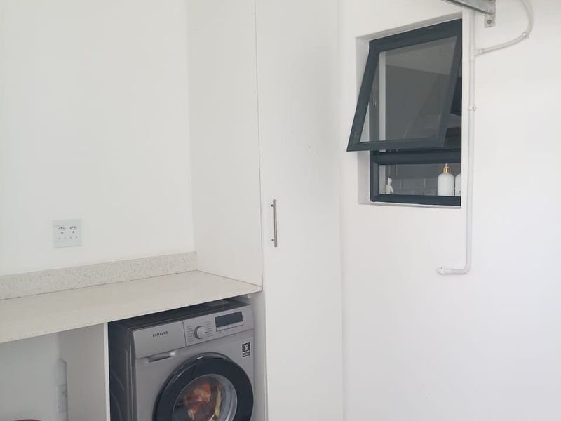 A clean and functional laundry area featuring built-in cabinetry, a stone countertop, tiled flooring, and an integrated air conditioning unit.
