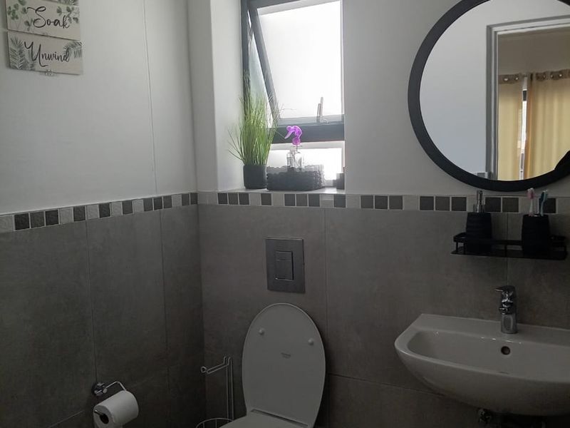 A modern bathroom featuring a wall-mounted toilet with a concealed cistern, a wall-hung basin with chrome fixtures, and neutral grey wall tiling.
