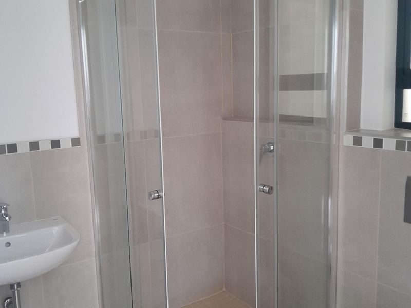 A clean and modern bathroom featuring a glass shower enclosure, wall-mounted basin, and toilet with neutral tiled finishes.