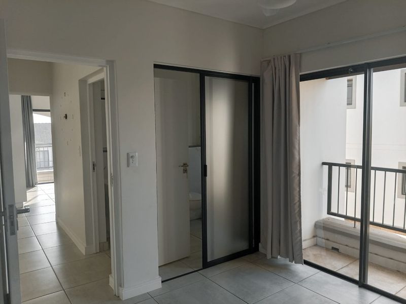 A bright, empty bedroom featuring tiled floors, a sliding glass door leading to a private balcony, and an en-suite bathroom entrance.