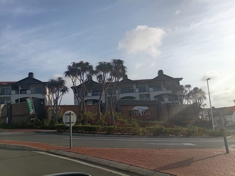 Street view of the entrance and exterior facade of the Zinga Estate apartment complex, featuring landscaped gardens and brick boundary walls.