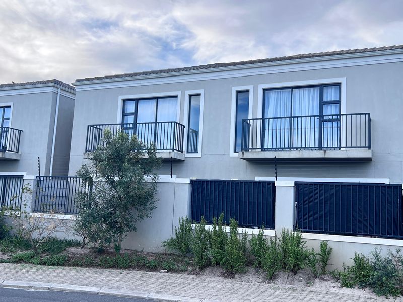 Front elevation of a modern townhouse complex featuring upper-level balconies with metal railings, sliding glass doors, and secure boundary walling with electric fencing.