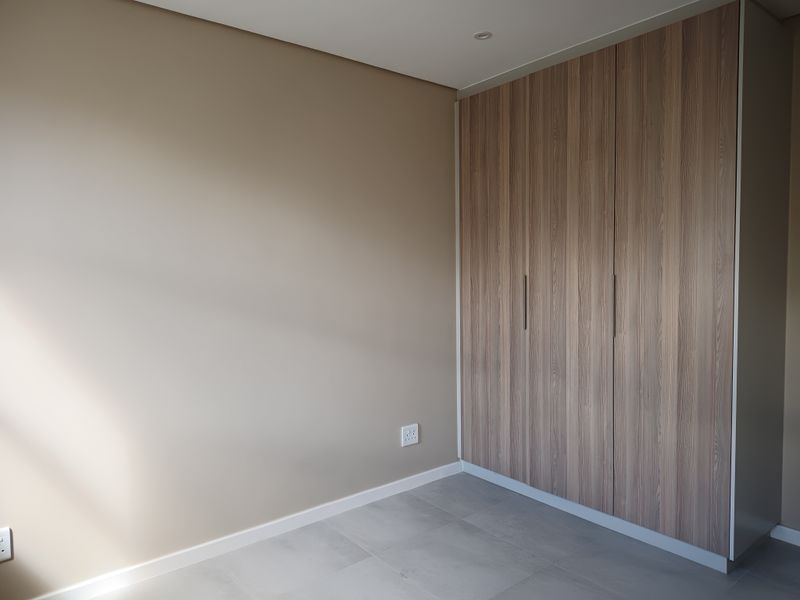 A clean, modern bedroom featuring neutral walls, large format floor tiles, and ample built-in wooden cabinetry.