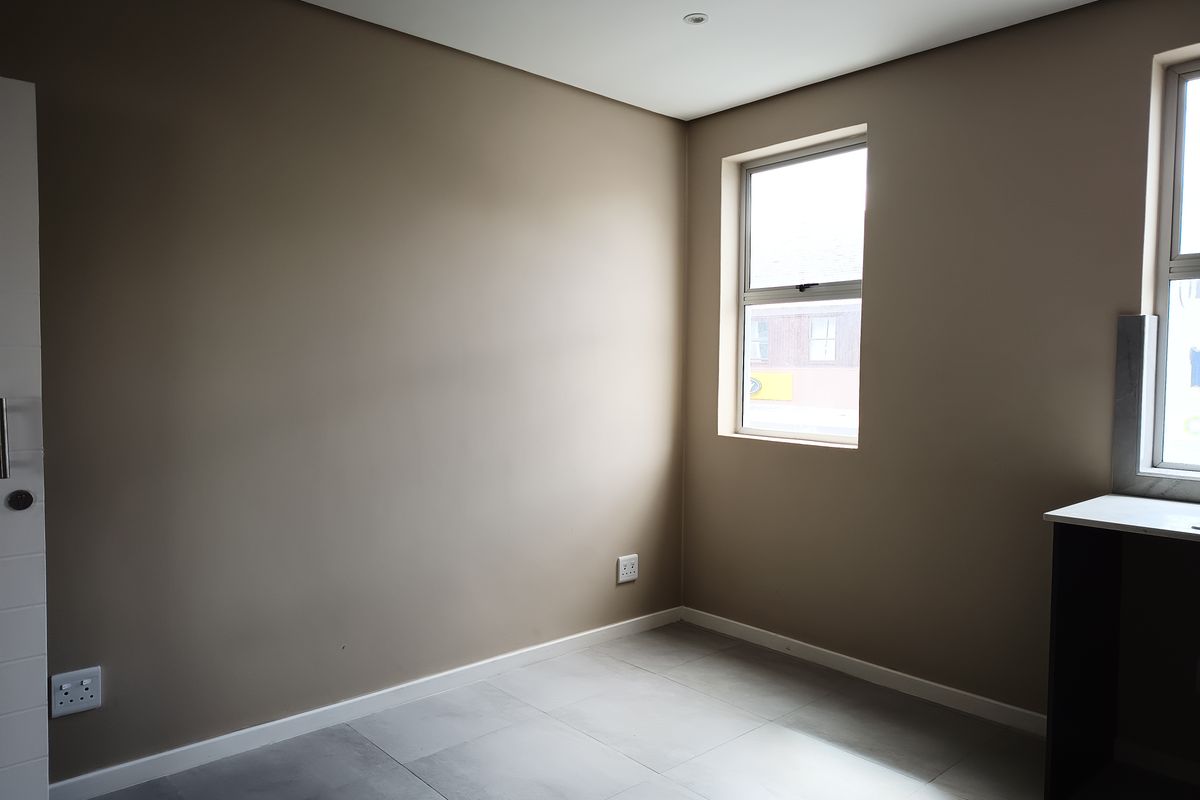 A clean, empty bedroom featuring neutral wall paint, modern tiled flooring, and natural light from the window.
