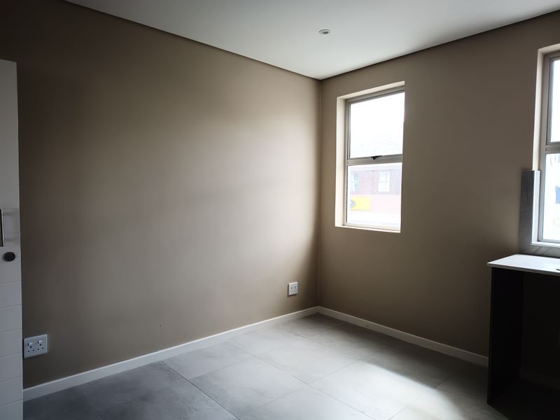 A clean, empty bedroom featuring neutral wall paint, modern tiled flooring, and natural light from the window.