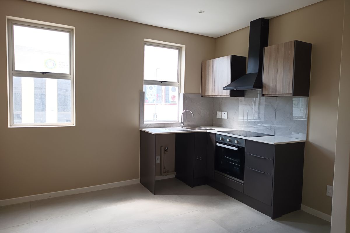 Modern kitchen featuring sleek dark cabinetry, stone countertops, integrated oven, hob, extractor fan, and a stainless steel sink with tiled splashback.
