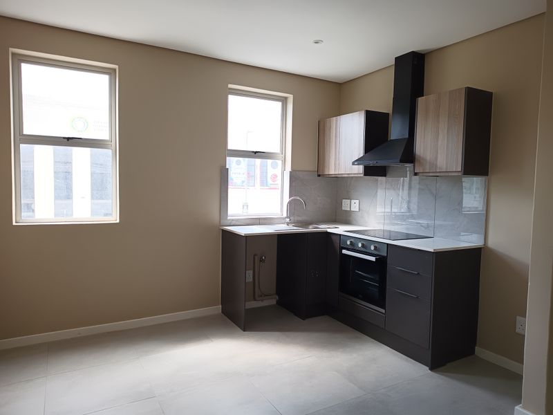 Modern kitchen featuring sleek dark cabinetry, stone countertops, integrated oven, hob, extractor fan, and a stainless steel sink with tiled splashback.