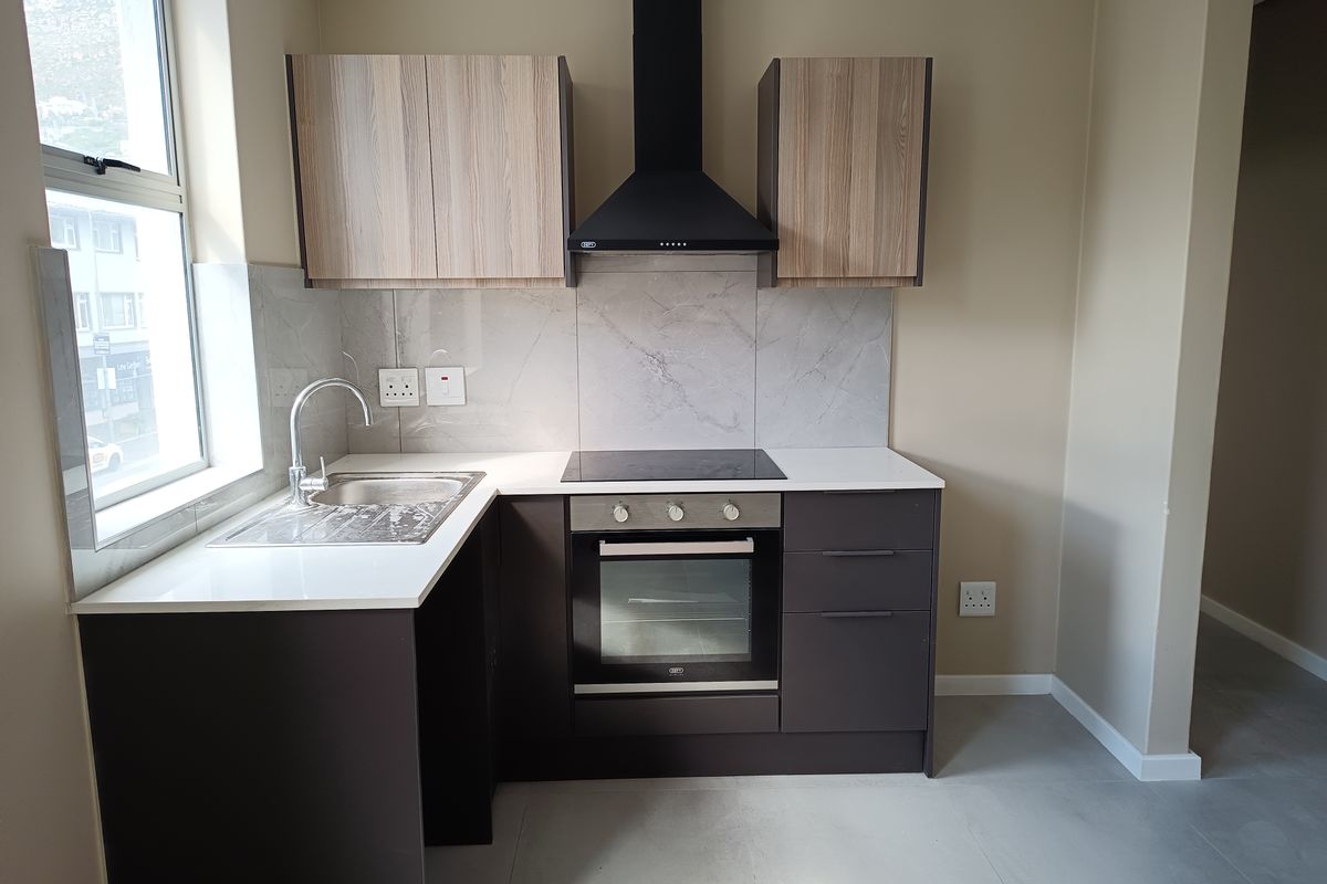 Modern kitchen featuring sleek dark cabinetry, stone countertops, integrated oven, electric hob, and a stylish tiled splashback in a clean, contemporary space.