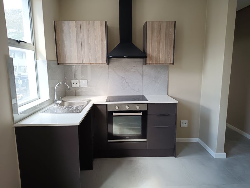 Modern kitchen featuring sleek dark cabinetry, stone countertops, integrated oven, electric hob, and a stylish tiled splashback in a clean, contemporary space.