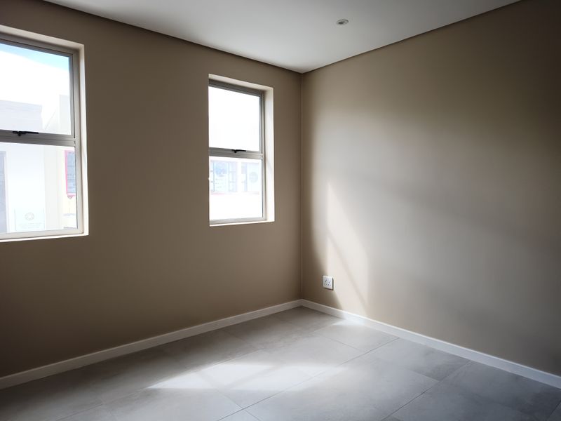 A bright, empty bedroom featuring neutral wall tones, modern tiled flooring, and large windows that provide ample natural light.