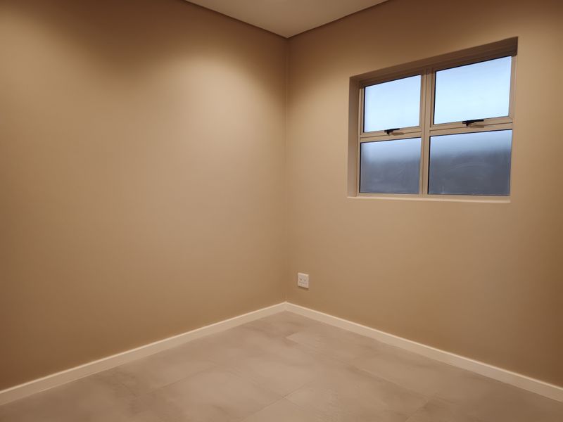 A clean, empty bedroom featuring neutral wall paint, tiled flooring, and an aluminium-framed window, providing a versatile space ready for furnishing.