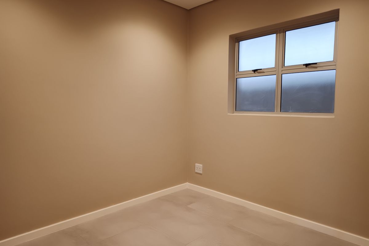 A clean, empty bedroom featuring neutral wall paint, tiled flooring, and an aluminium-framed window, providing a versatile space ready for furnishing.