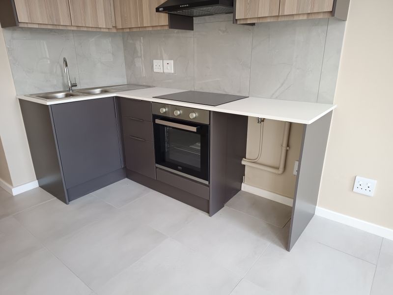 Modern kitchen featuring sleek grey cabinetry, stone countertops, integrated oven and hob, and a contemporary tiled splashback in a clean, minimalist space.