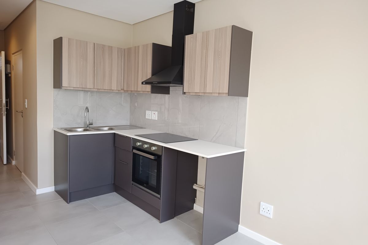 Modern kitchen featuring sleek grey and wood-tone cabinetry, stone countertops, integrated oven, hob, and extractor fan with a clean tiled splashback.