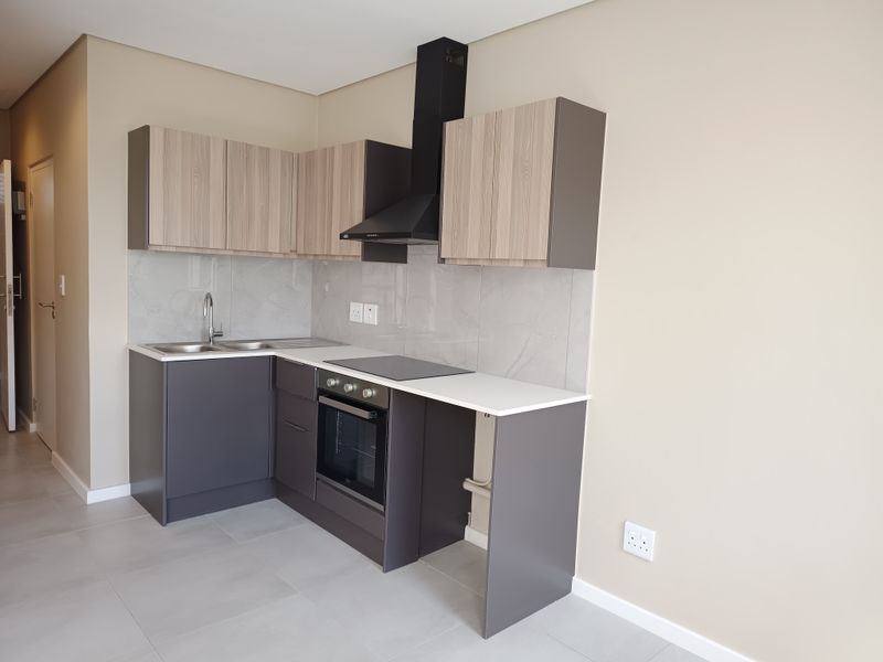 Modern kitchen featuring sleek grey and wood-tone cabinetry, stone countertops, integrated oven, hob, and extractor fan with a clean tiled splashback.